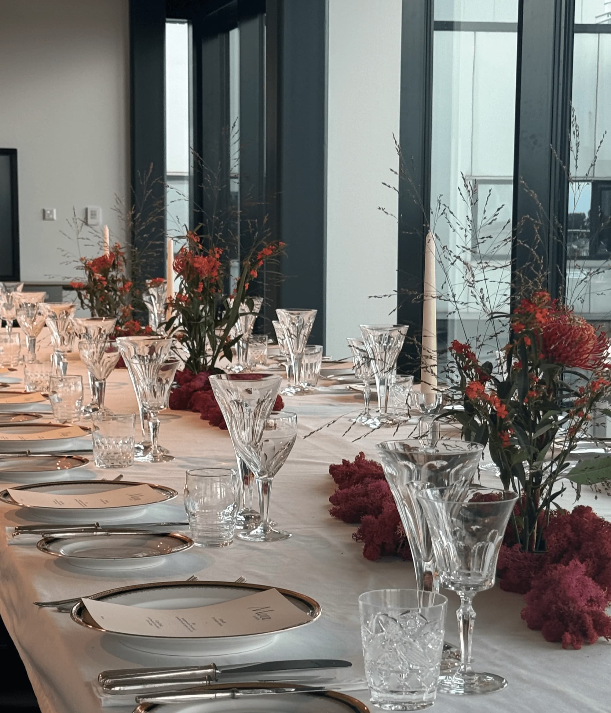 Lange gedekte tafel met kristallen glazen, zilver en rode bloemen