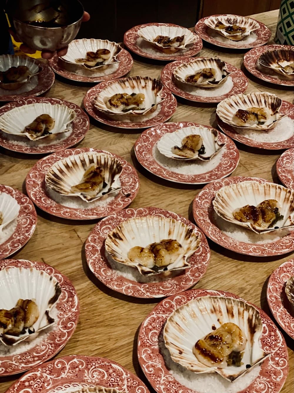 Rijen sintjakobsschelpen met een gegrilde hap op roodgebloemde borden